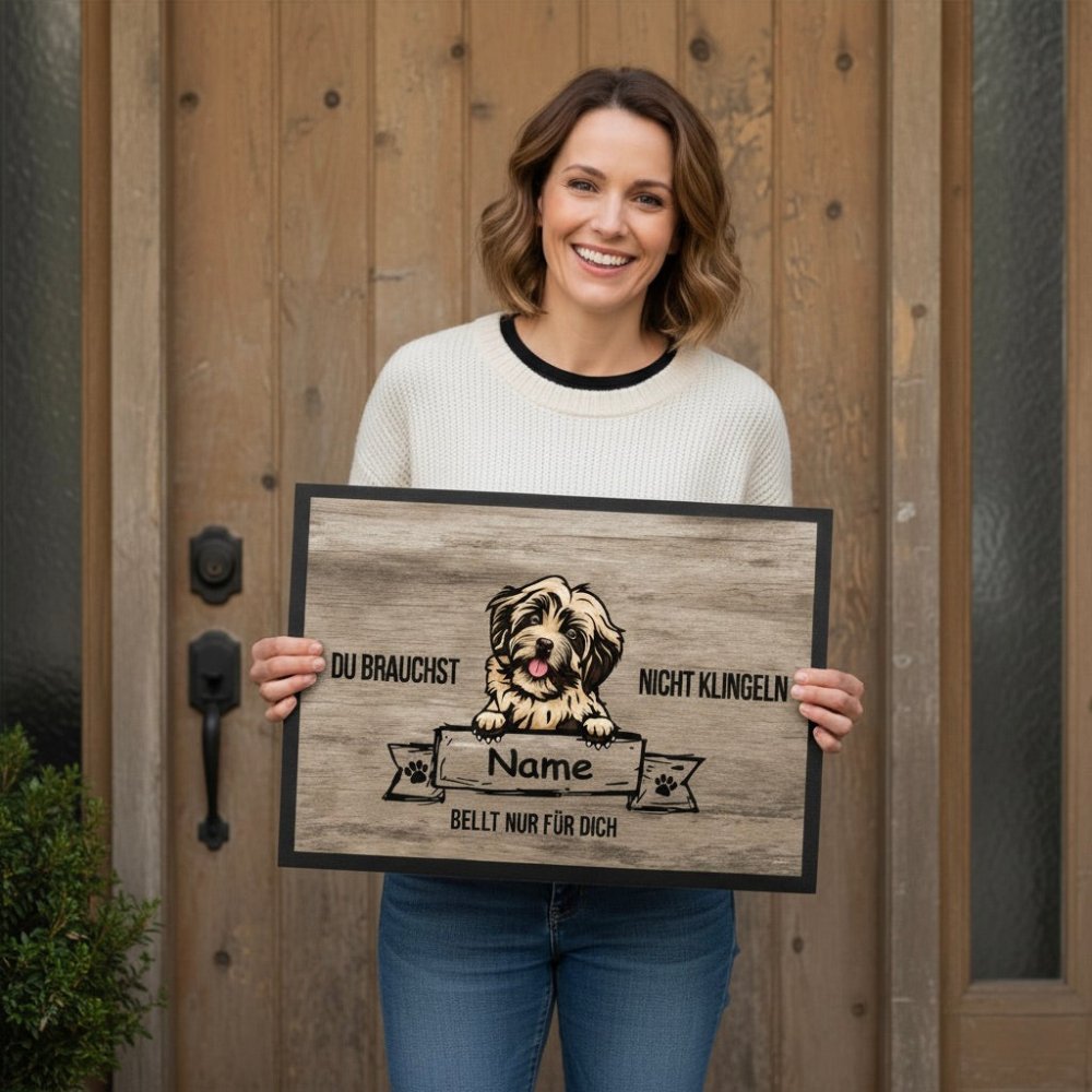Frau steht vor  Haustür und hält eine Fußmatte in den Händen. Auf der Matte steht: Du brauchst nicht klingeln ...bellt für Dich