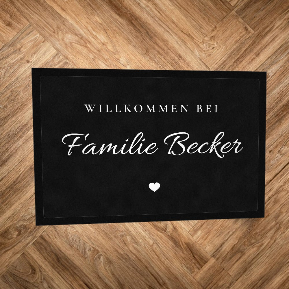 Fußmatte „Willkommen bei Familie Becker“ in Schreibschrift mit kleinem Herz, auf Parkettboden