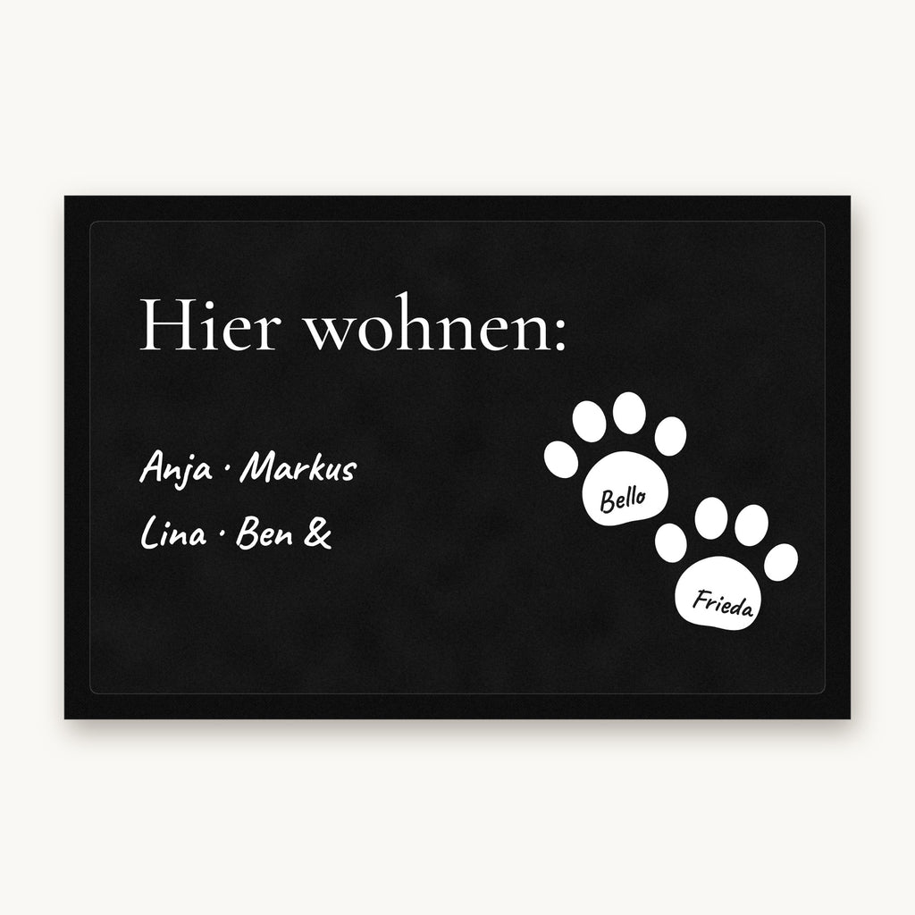 Fußmatte „Hier wohnen“ mit Familiennamen und zwei weißen Pfoten mit Hundenamen, Mattenfarbe Schwarz