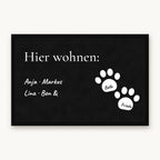 Fußmatte „Hier wohnen“ mit Familiennamen und zwei weißen Pfoten mit Hundenamen, Mattenfarbe Schwarz