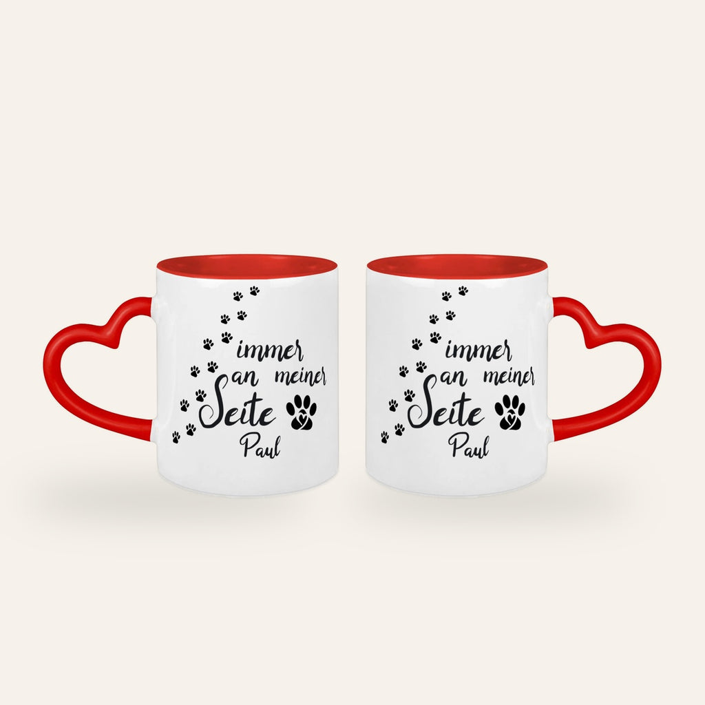 Weiße Tasse mit rotem Herzhenkel, dem Spruch Immer an meiner Seite, Pfotenspuren und dem Namen Paul, Ansicht beider Seiten