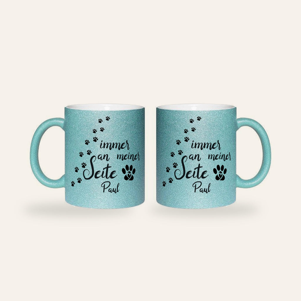 Hellblaue Glitzertasse mit dem Spruch Immer an meiner Seite, Pfotenspuren und dem Namen Paul, Ansicht beider Seiten
